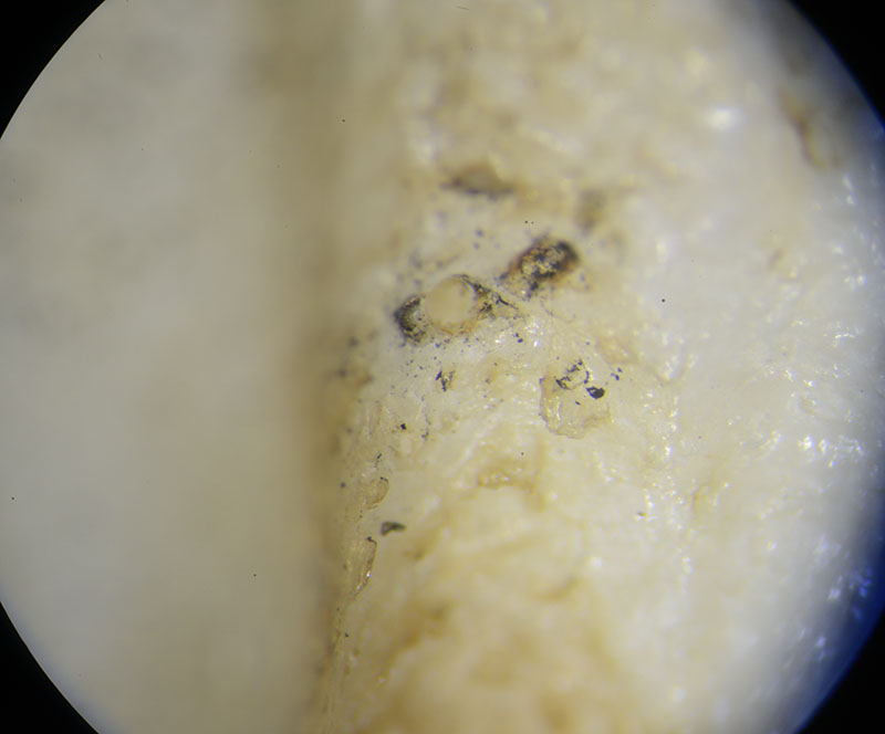 The result of the hot pin test on the mystery sample under magnification. The pin melted a deep recess in the surface with blackened edges.